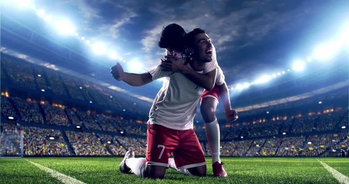 Professional footballer is happy and slides with his hands to the air. Another soccer player runs after him happily. Action takes place on soccer stadium.  Stadium and crowd are made in 3D.