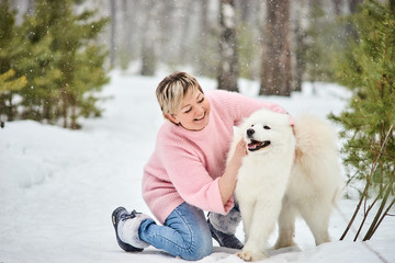 Woman in the winter forest walking with a dog. Snow is falling