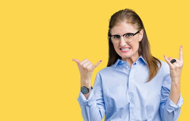 Beautiful middle age mature business woman wearing glasses over isolated background shouting with crazy expression doing rock symbol with hands up. Music star. Heavy concept.