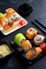 Various Fresh and delicious sushi set on black slate with slate sticks, sauce and nori on black stone background , flat lay