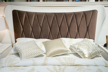 Bed with a big brown soft headboard and pillows. Close-up