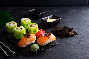 Various Fresh and delicious sushi set on black slate with slate sticks, sauce and nori on black stone background , flat lay