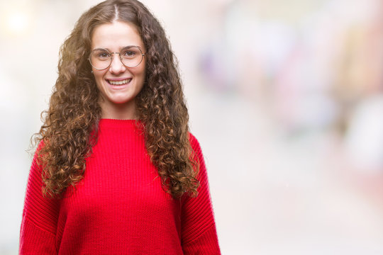 Beautiful brunette curly hair young girl wearing glasses and winter sweater over isolated background with a happy and cool smile on face. Lucky person.