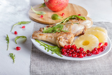 Fried chicken legs with rucola, pineapple and pomegranate seeds on white wooden background.