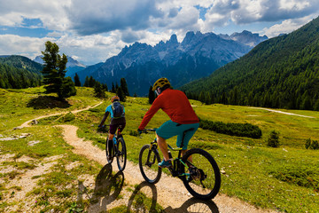 Cycling woman and man riding on bikes in Dolomites mountains andscape. Couple cycling MTB enduro...