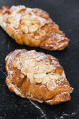 Two fresh croissant with almond cream on marble black background. Close up