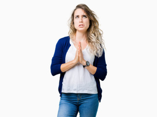 Beautiful young blonde woman over isolated background begging and praying with hands together with hope expression on face very emotional and worried. Asking for forgiveness. Religion concept.