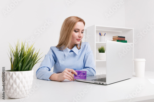 Office woman holding purple credit card and making shopping online at her workplace