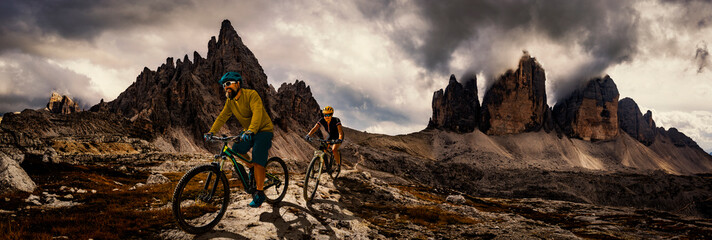 Fototapeta na wymiar Cycling woman and man riding on bikes in Dolomites mountains andscape. Couple cycling MTB enduro trail track. Outdoor sport activity.
