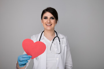 Woman in a white coat with stethoscope around neck holding image of heart