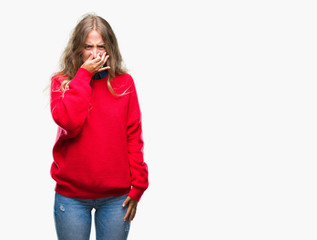 Beautiful young blonde woman wearing winter sweater over isolated background smelling something...