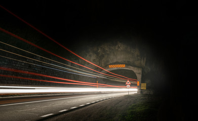 Fototapeta na wymiar A long exposure photo showing the entrance to the tunnel in mountain with lots of light tails and several traffic signs along the road by night.