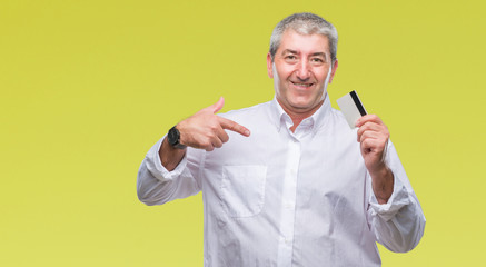 Handsome senior man holding credit card over isolated background with surprise face pointing finger to himself