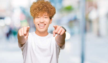 Young handsome man with afro hair wearing casual white t-shirt Pointing to you and the camera with fingers, smiling positive and cheerful