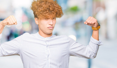 Young handsome business man with afro hair wearing elegant shirt showing arms muscles smiling proud. Fitness concept.