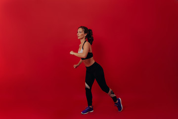 Fototapeta na wymiar Side view of sporty woman wearing sport uniform against red background. Female athlete preparing for running 