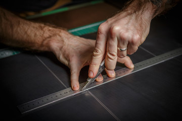 man working as artisan in his leather workshop, cutting leather by knife