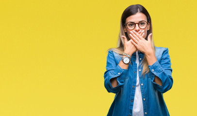 Young beautiful woman over wearing glasses over isolated background shocked covering mouth with hands for mistake. Secret concept.