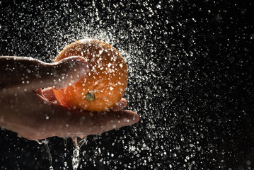 Orange in male hand under the stream of water