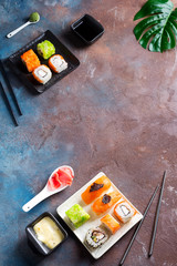 Various Fresh and delicious sushi set on black slate with slate sticks, sauce and nori on duotone stone background , flat lay