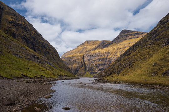 Scenic landscape Picture of wild river or creek between high mountains without trees in village Saksun Faroese island Streymoy during the sunny spring morning. Scandinavian nature in North Atlantic.