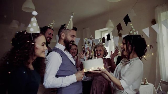 A portrait of multigeneration family with a cake on a indoor birthday party, confetti falling.