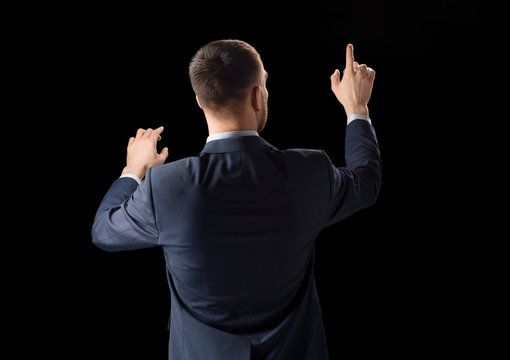 business, technology and augmented reality concept - businessman in suit working with invisible virtual screen over black background