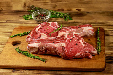 Fototapeta premium Raw fresh beef rib eye steaks on bone with spices and rosemary on wooden table
