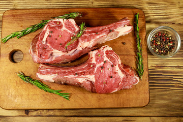 Raw fresh beef rib eye steaks on bone with spices and rosemary on wooden table. Top view