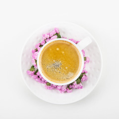 White cup of coffee on a white table with pink flowers of dried flower. Minimalism. Top view, flat lay