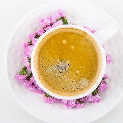 White cup of coffee on a white table with pink flowers of dried flower. Minimalism. Top view, flat lay