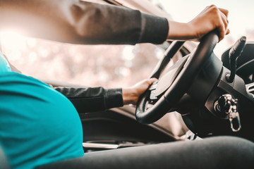 Close up of pregnant Caucasian woman driving car. Both hands on steering wheel.
