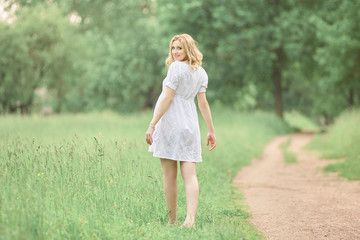rear view. pregnant woman walking barefoot on grass.
