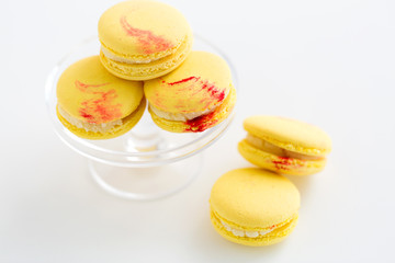 sweets, pastry and food concept - close up of lemon yellow macarons on glass confectionery stand over white background