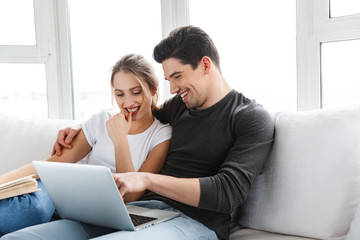 Photo of modern couple using silver laptop while sitting on couch in bright room at home