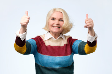 cheerful old woman in colored sweater showing thumbs up gesture