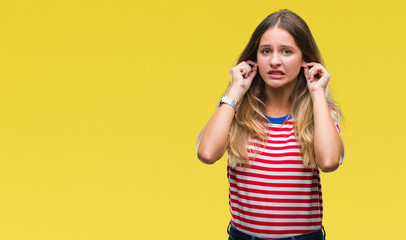 Young beautiful blonde woman over isolated background covering ears with fingers with annoyed expression for the noise of loud music. Deaf concept.