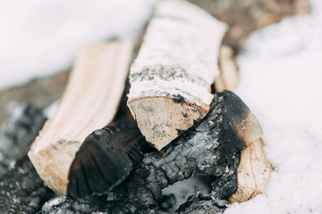 Stack of birch wood in the snow. Extinguished fire and coals on the boards.