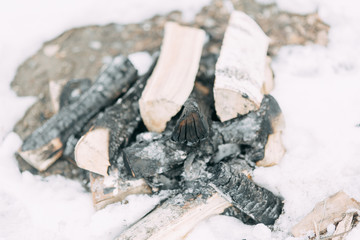 Stack of birch wood in the snow. Extinguished fire and coals on the boards.