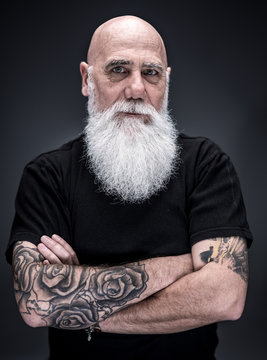 studio portrait of a bald man with tattooed arms and white beard