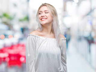 Young blonde woman over isolated background looking away to side with smile on face, natural expression. Laughing confident.