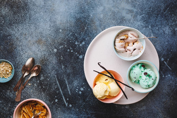 Colorful ice cream in colored bowls with spoons on rustic wooden background , blank space