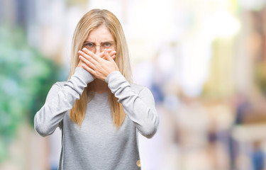 Young beautiful blonde woman wearing glasses over isolated background shocked covering mouth with hands for mistake. Secret concept.