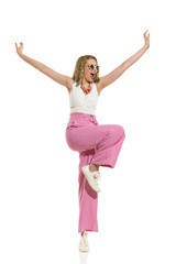 Happy Woman In Striped Wide Legs Trousers Is Standing On One Leg With Arms Outstretched And Shouting