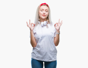 Young blonde woman wearing headphones listening to music over isolated background relax and smiling with eyes closed doing meditation gesture with fingers. Yoga concept.