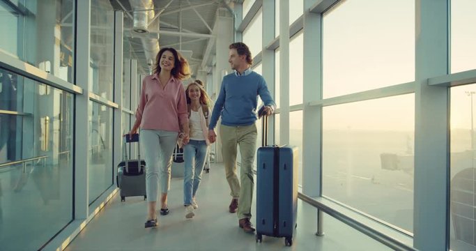 Happy caucasian family with a daughter walking the airport corridor with suitcases and smiling.