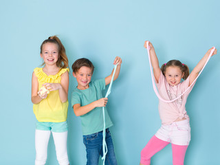 two beautiful and funny girls and one cool boy playing with a lot of slime in front of blue...