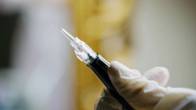 A beautician holds in her hand a pen for permanent makeup and checks it before the procedure. Close-up. Blurred background. Beauty industry.