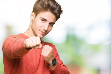 Young handsome man over isolated background Punching fist to fight, aggressive and angry attack, threat and violence