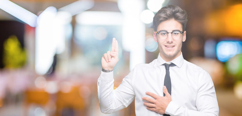 Young business man wearing glasses over isolated background Swearing with hand on chest and...
